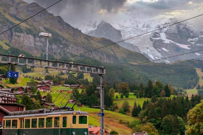 Un train de montagne jaune et vert circule dans un paysage alpin spectaculaire.