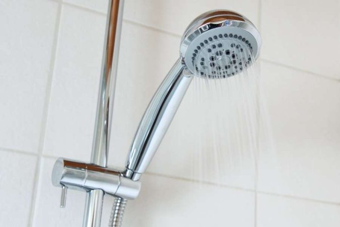 Gros plan sur un pommeau de douche chromé moderne fixée à une barre de douche, avec de l'eau qui coule.