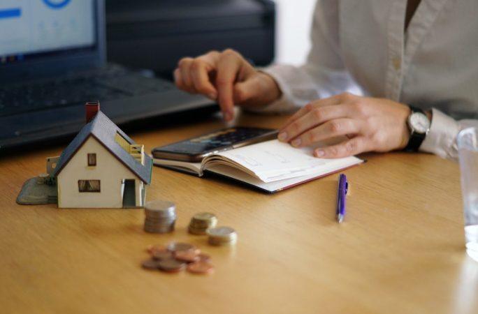Calcul du budget immobilier avec maquette de maison, pièces de monnaie et analyse de l'impact charges copropriété prix vente.