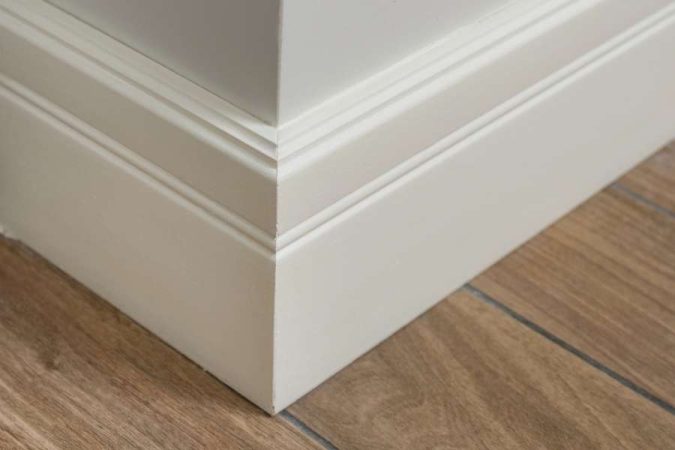 Des baguettes d'angle blanches fixées proprement le long des plinthes au coin d'un mur.